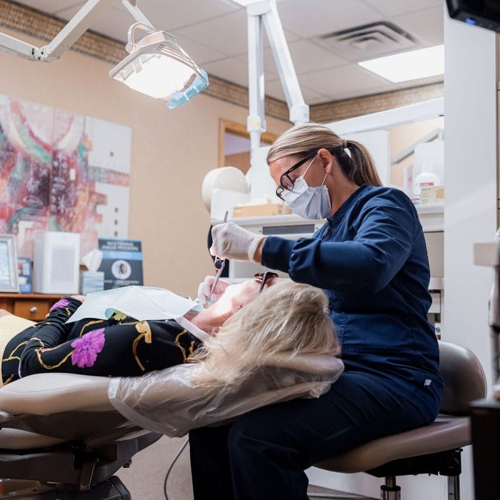 A dentist from Dental Peak Arts fitting a patient with an Invisalign aligner. The dentist is carefully positioning the clear aligner over the patient's teeth while the patient sits reclined in the dental chair.