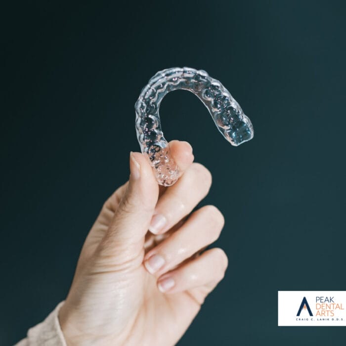 A close-up image of a hand holding an Invisalign clear aligner, showcasing the transparent and flexible nature of the dental device.