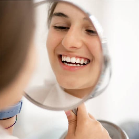 Smiling woman looking at her teeth in a handheld mirror, highlighting a bright, healthy smile